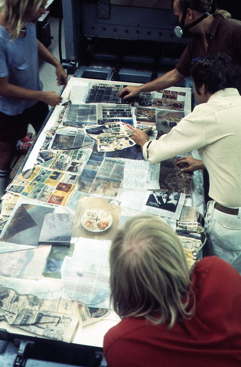 photograph from above of figures around a table with colorful magazines spread out on fabric