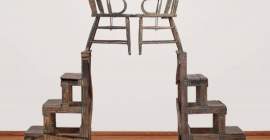A sculpture made of two symmetrical wood and metal stands each with a wooden chair on top.