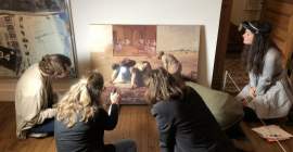 A group of five people sitting on the floor looking intently at an artwork depicting iconic paintings of Western art history. 
